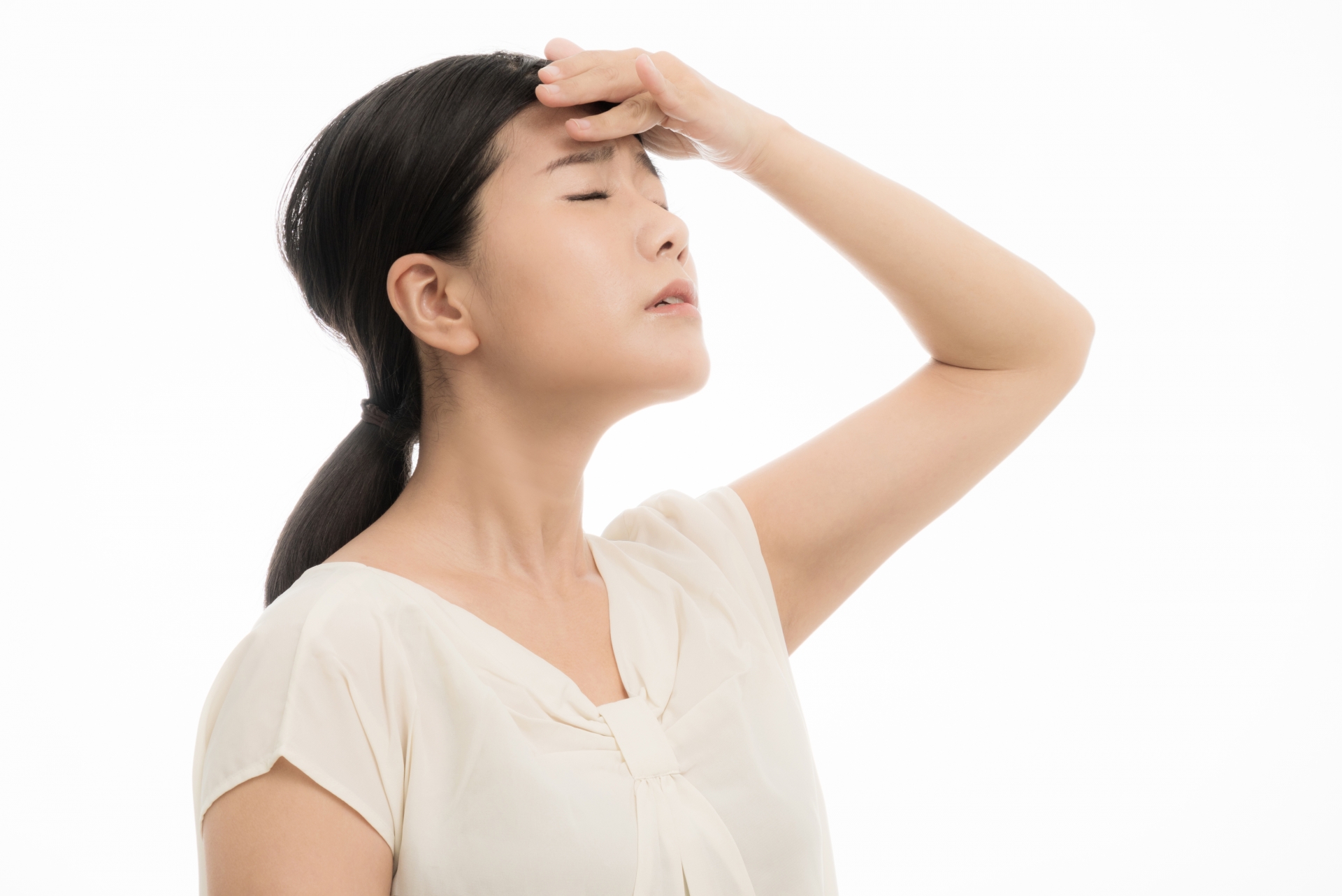 頭痛で額を押さえ、つらそうな表情をしている女性