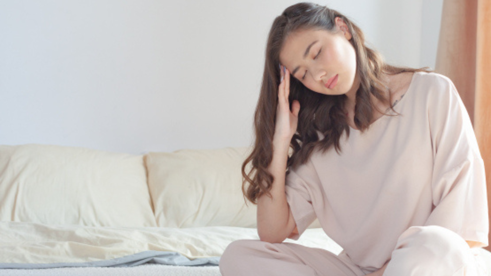 朝起きても頭痛がつらく、ベッドで頭を押さえる女性
