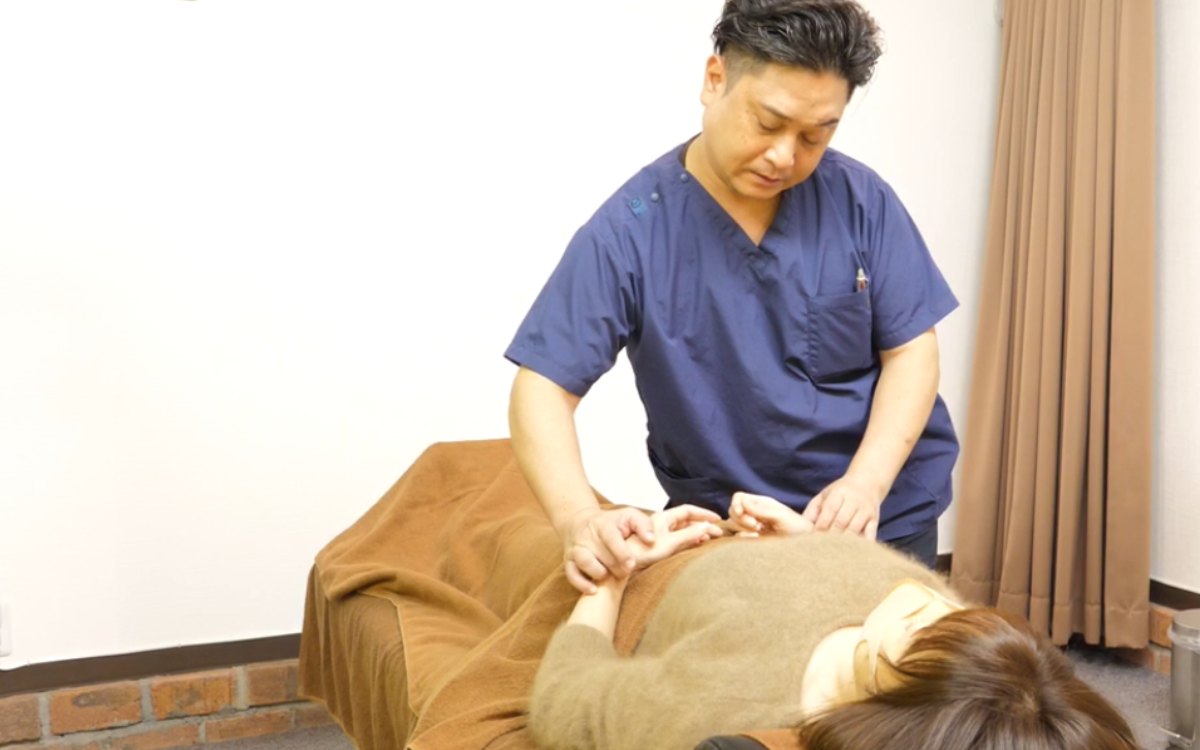 鍼灸師が患者の腕に優しく指を添え、脈診で体の状態を確認している様子