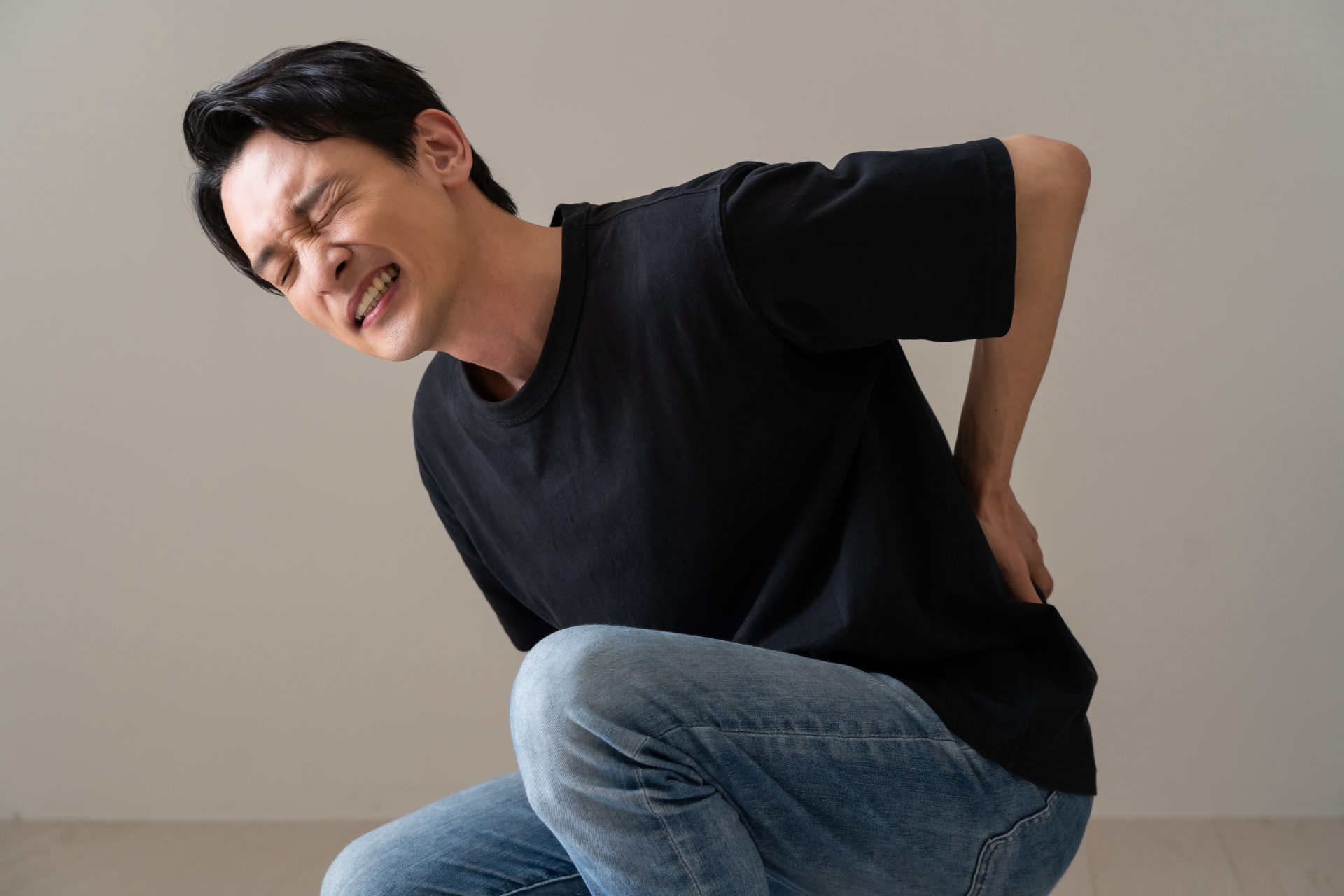ぎっくり腰を発症し、激痛で動けなくなったイメージ。腰に手を当てて苦悶の表情を浮かべる黒いTシャツの男性