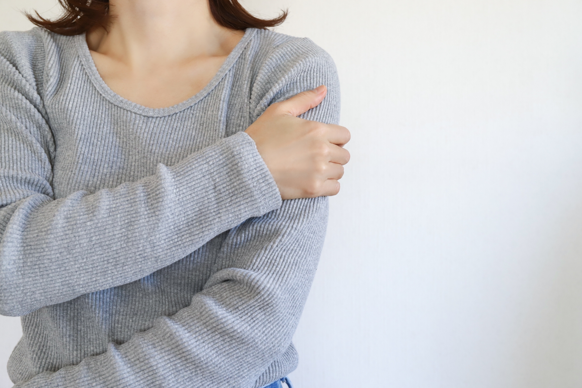 腕を押さえて痛みを感じている女性。上肢痛・腕のしびれ・だるさのイメージ