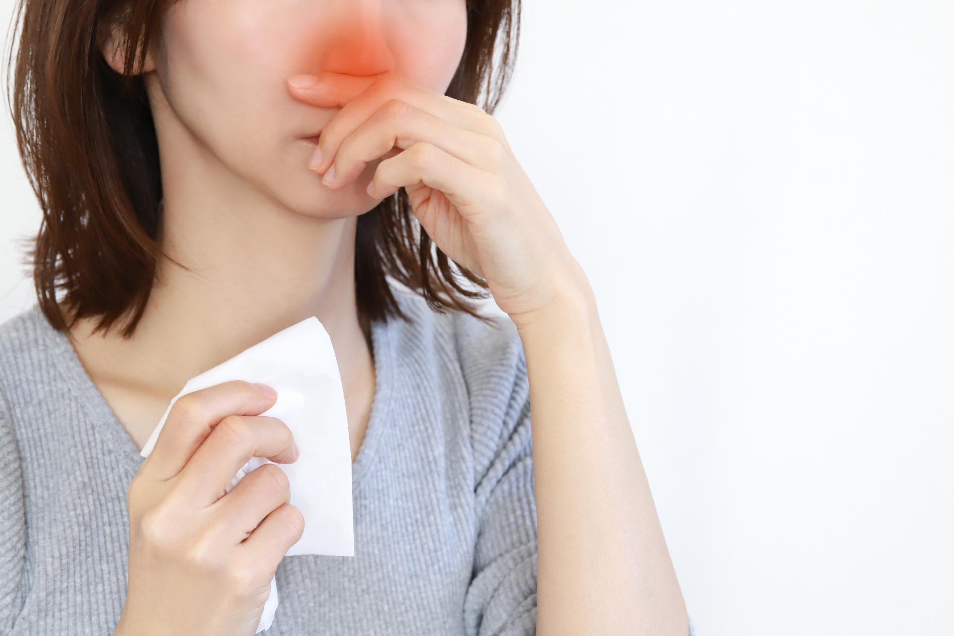 ティッシュを手に鼻を押さえる女性。鼻炎・花粉症による鼻づまりやくしゃみのイメージ
