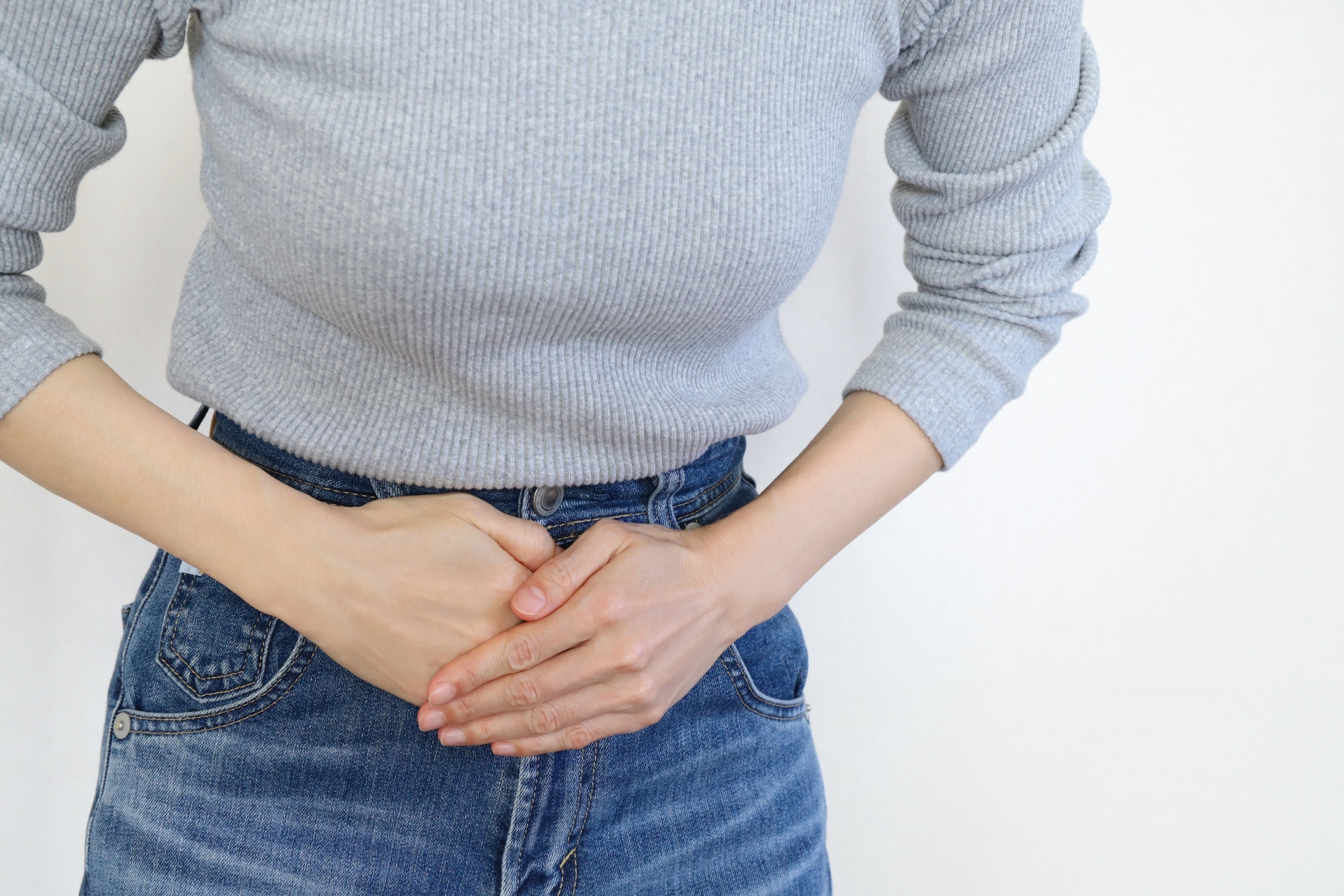 下腹部に手を当てる女性。過敏性腸症候群による腹痛やお腹の不調のイメージ