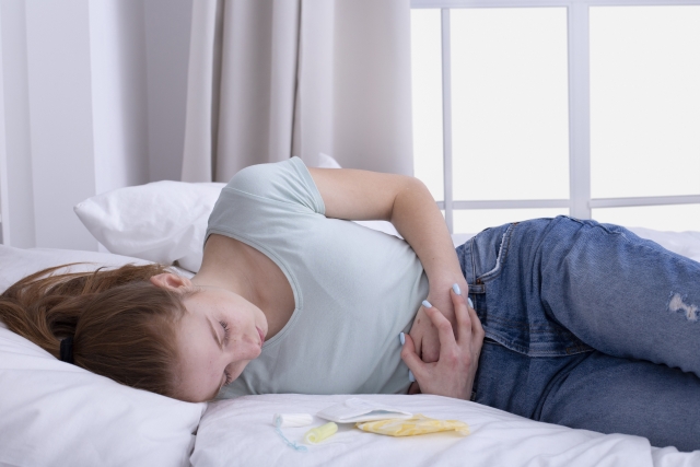 ベッドで腹部を押さえてうずくまる女性。生理痛のイメージ