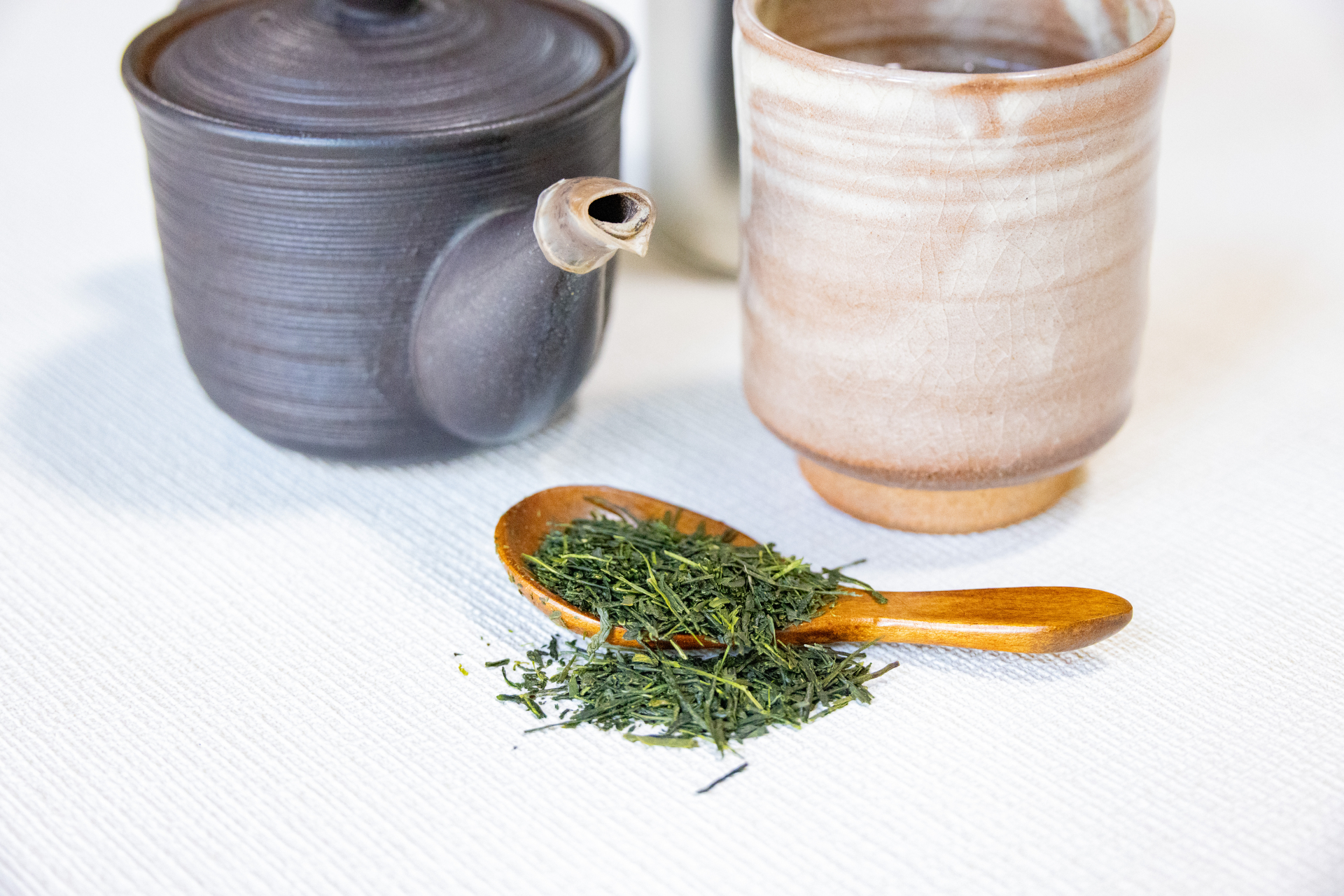 急須と湯呑みの手前に、木のさじにのせた緑茶の茶葉